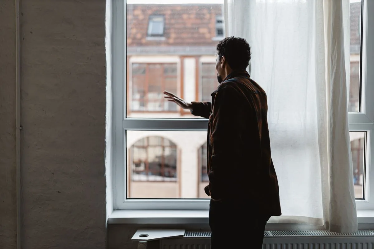 Person standing by a window in quiet reflection while processing grief